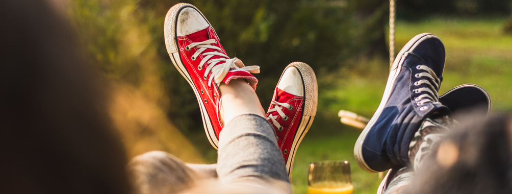 Zwei Paar hochgelegte Füße mit Chucks in Rot und Blau.