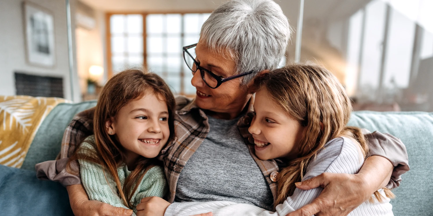 Oma umarmt ihre zwei Enkelinnen auf dem Sofa