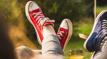 Zwei Paar hochgelegte Füße mit Chucks in Rot und Blau.