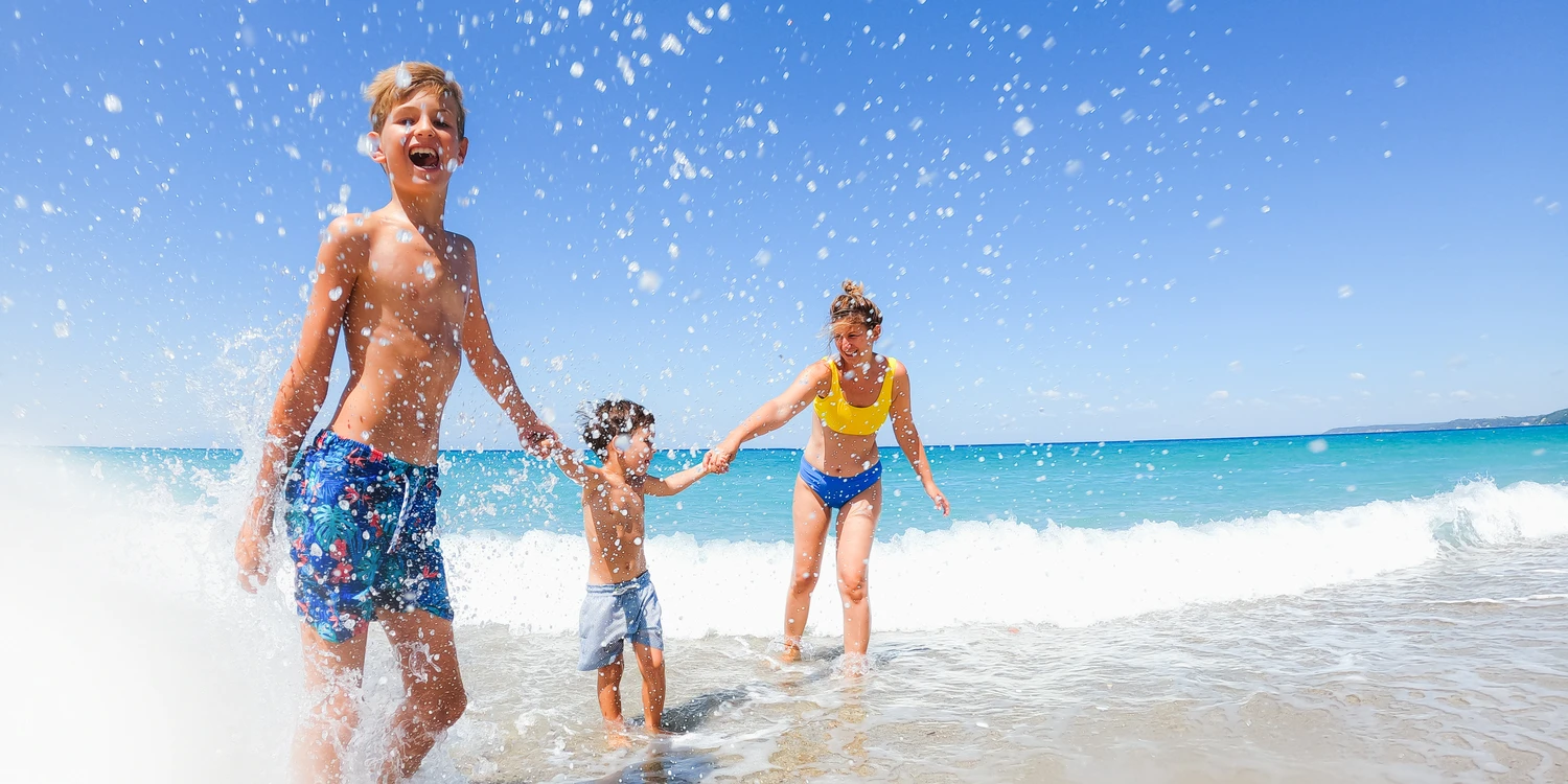 Spaß im Sommerurlaub Zwei Kinder und ihre Mutter am Strand