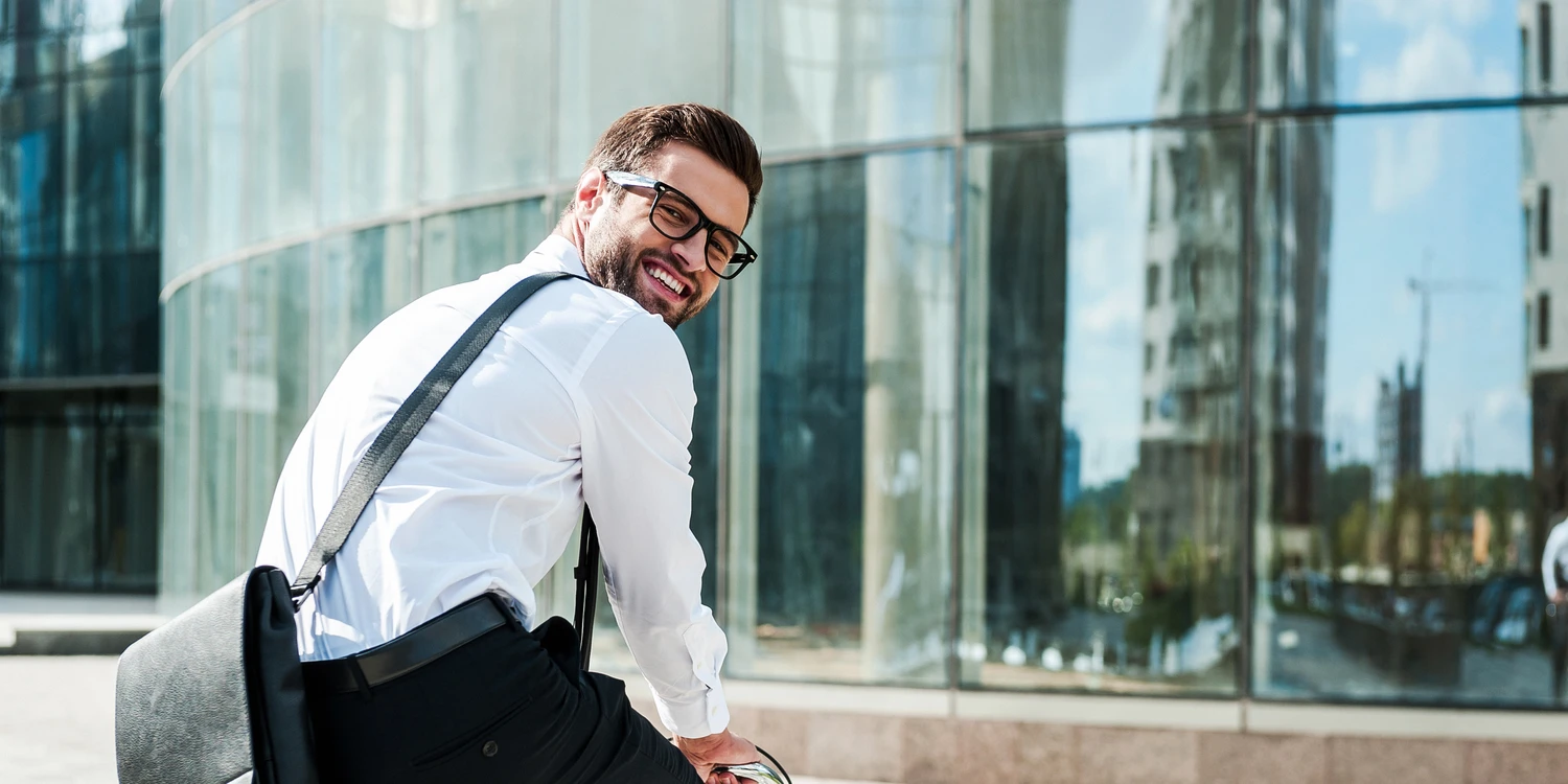 Junger Mann auf dem Fahrrad vor einer Glasfassade schaut sich um