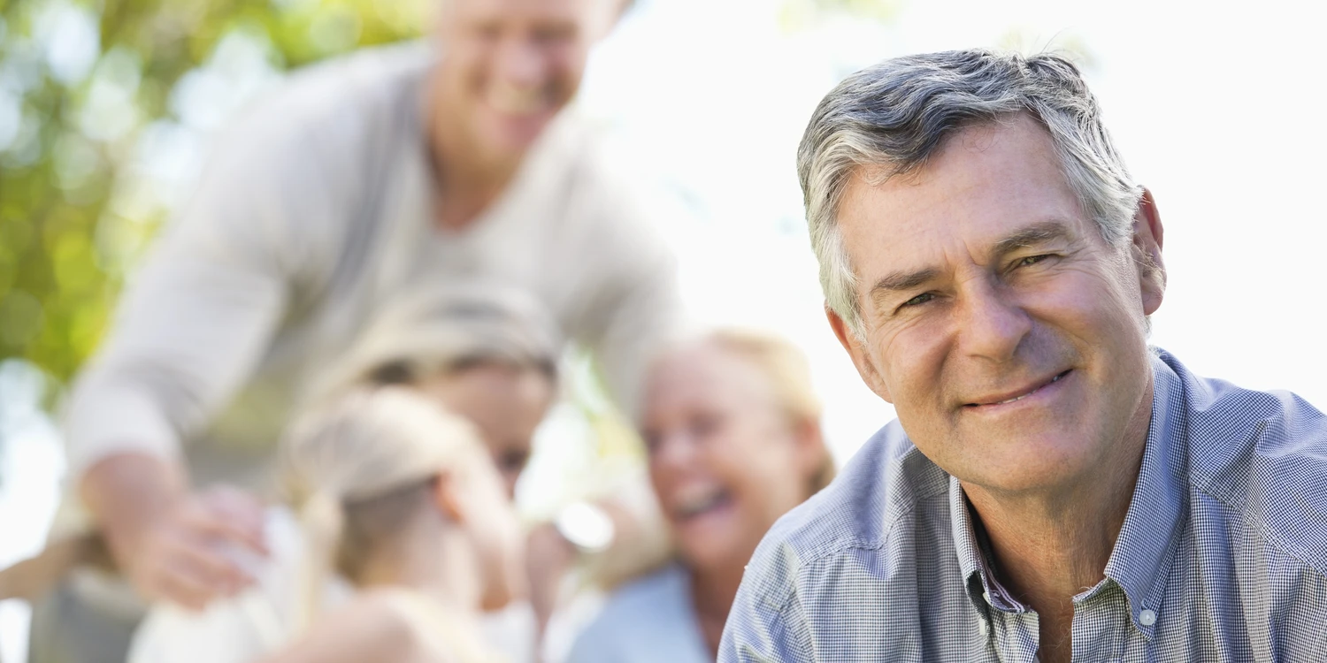 Erwachsener Mann schaut in die Kamera. Im Hintergrund sind weitere Personen.