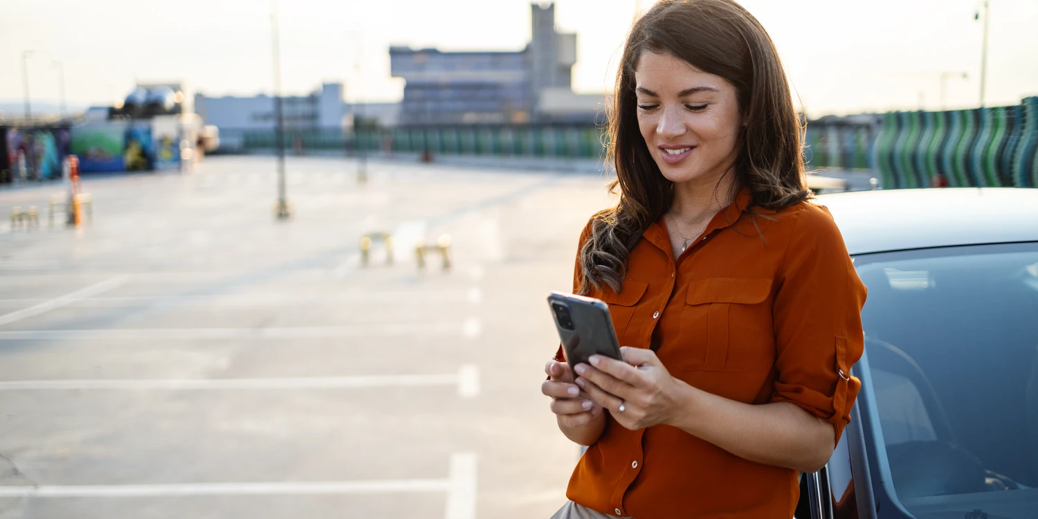 Frau mit Mobiltelefon Frau mit Mobiltelefon an ihrem Auto auf den Flughafenparkplatz