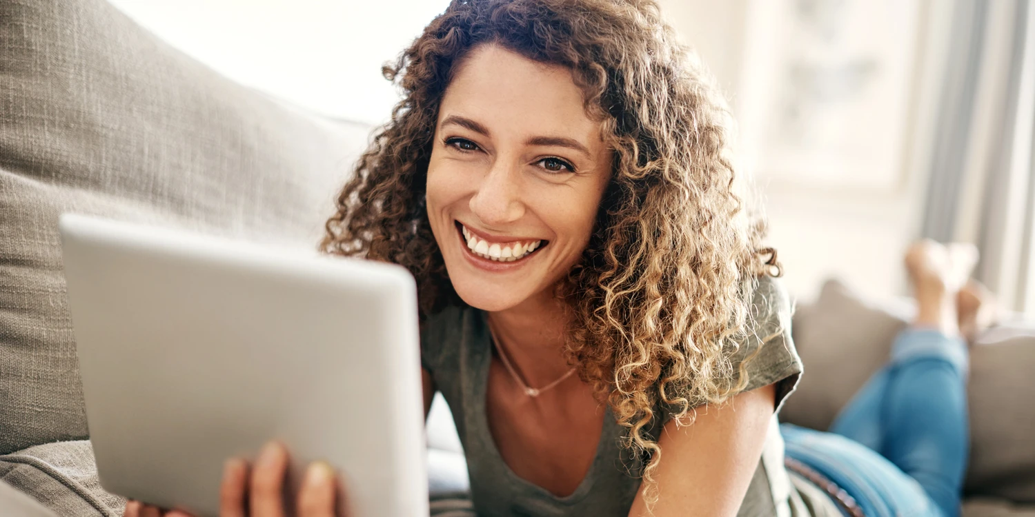 Frau liegt mit einem Notepad auf dem Sofa