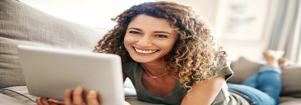 Frau liegt mit einem Notepad auf dem Sofa